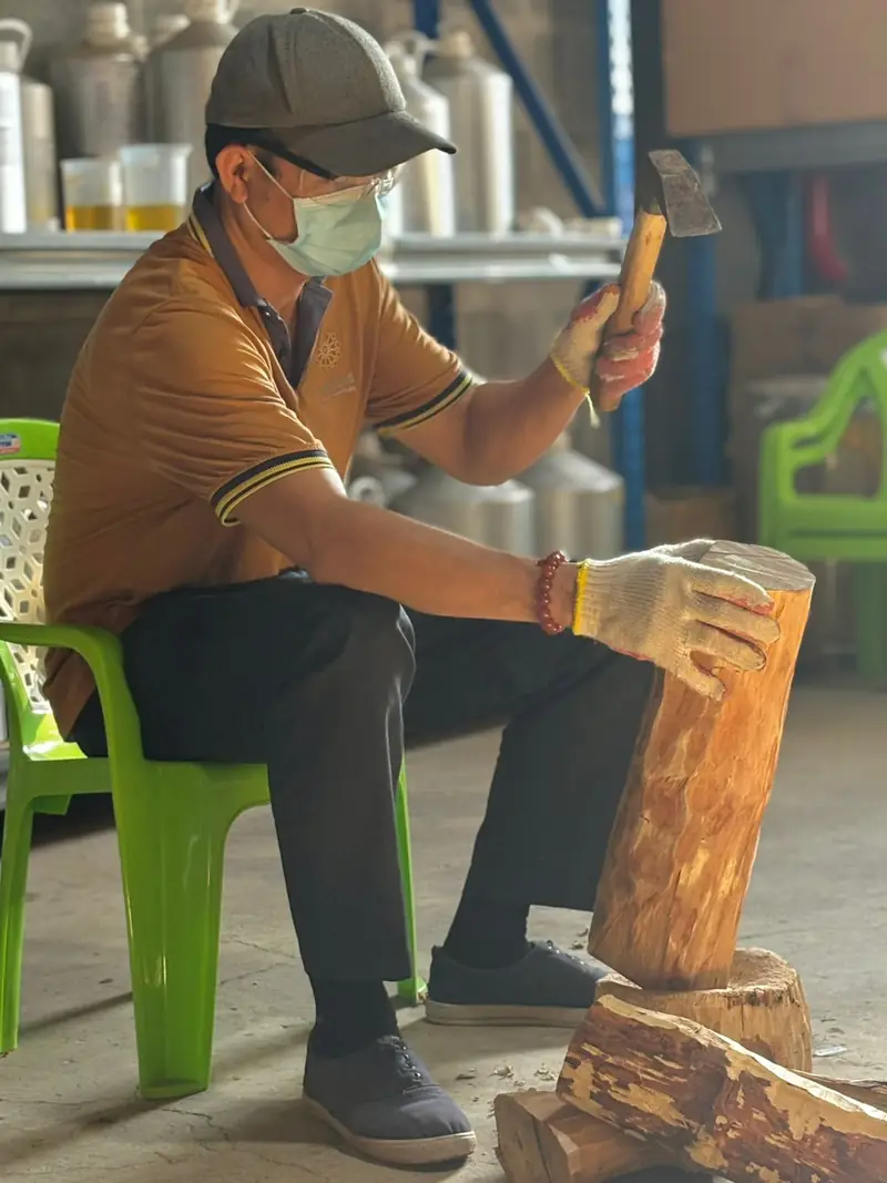 A Marigold craftsman desapping a sandalwood log by hand with a mallet